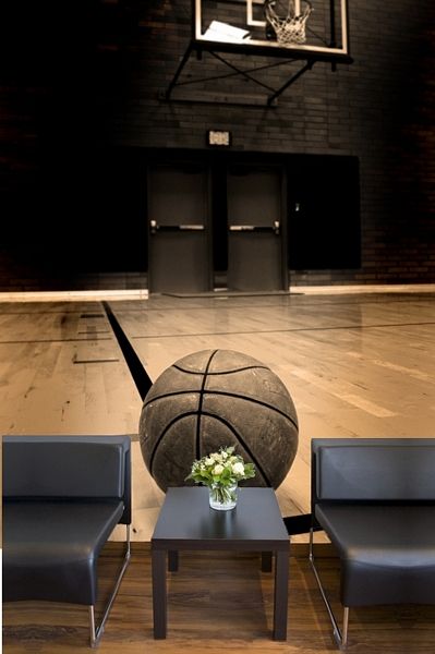 fototapeta z piłką do koszykówki na tle hali sportowej za dwoma czarnymi fotelami i stolikiem z bukietem kwiatów