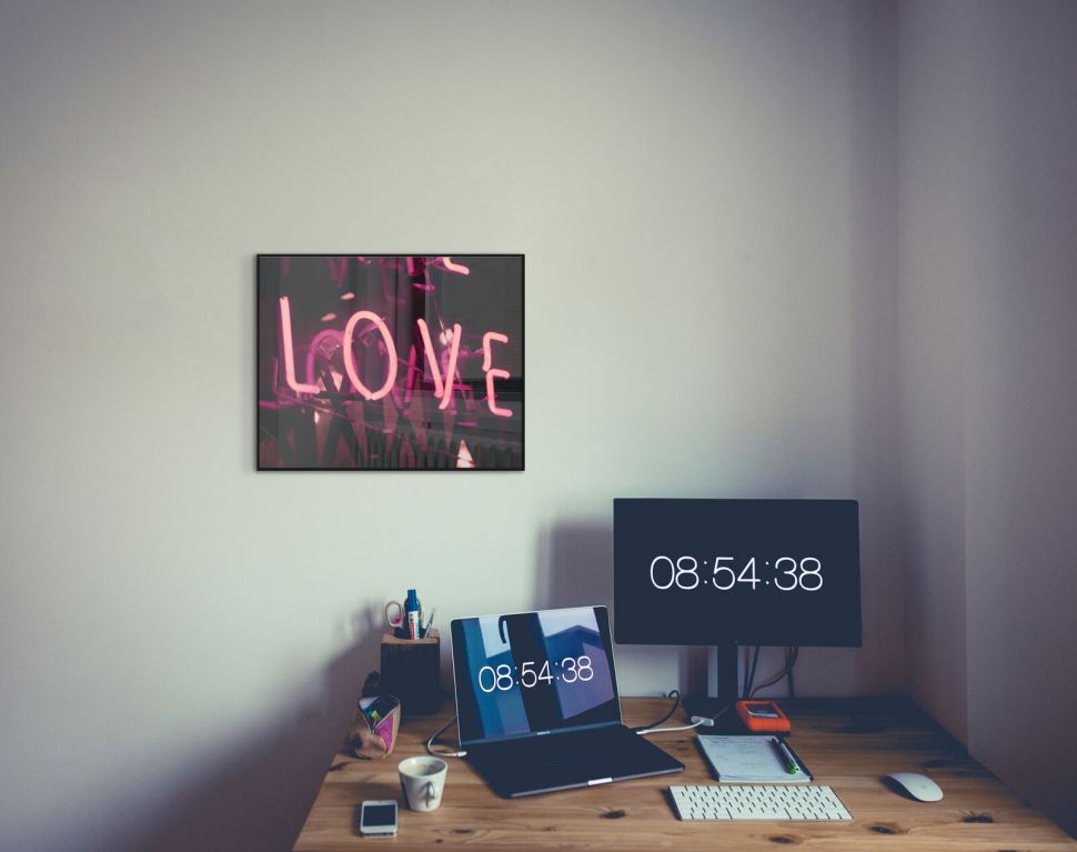 Plakat z napisem neonowym Love w czarnej ramce powieszony nad biurkiem